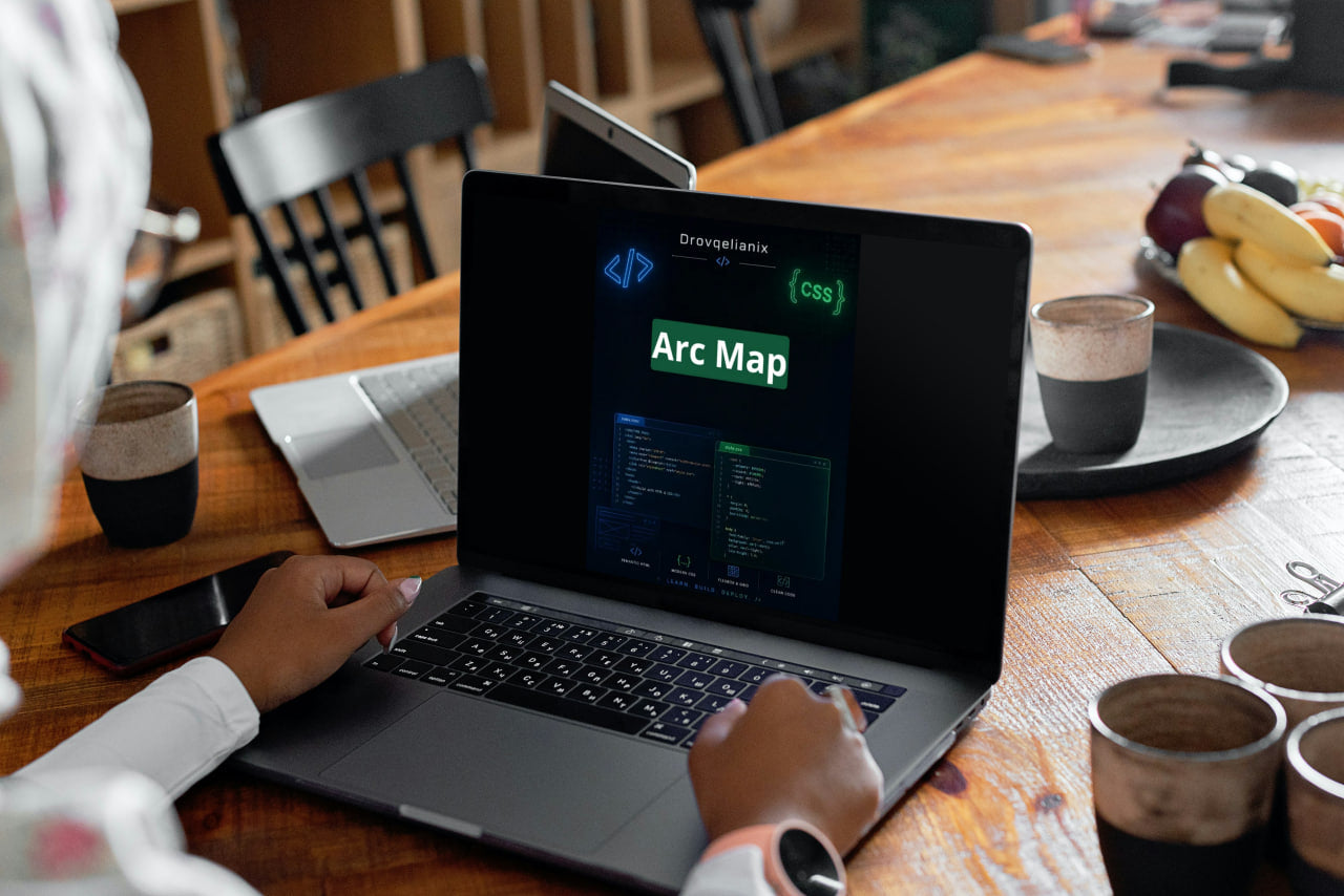 A person uses a black laptop on a wooden table, with the screen displaying a software interface labeled 'Disruptivity' and 'Arc Map'. The scene is set in a warm, modern workspace with coffee cups, a phone, and fruit on the table.